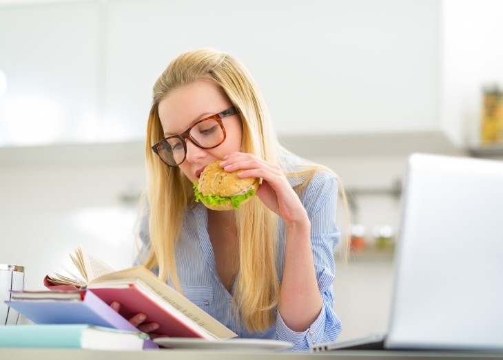 Young woman eating sandwich while studying in kitchen